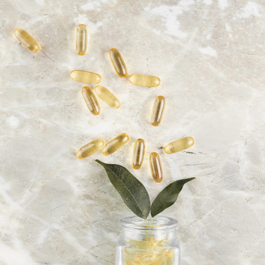 Omega-3 fish oil capsules spilling from a glass jar with green leaves on a marble background