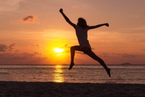 Silhouette of a woman jumping on a beach at sunset with the ocean in the background