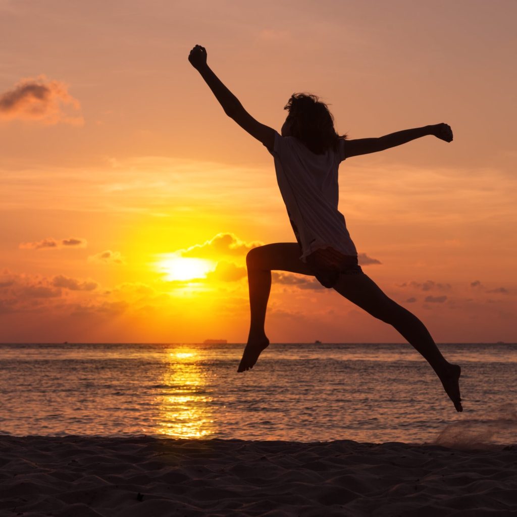 Silhouette of a woman jumping on a beach at sunset with the ocean in the background