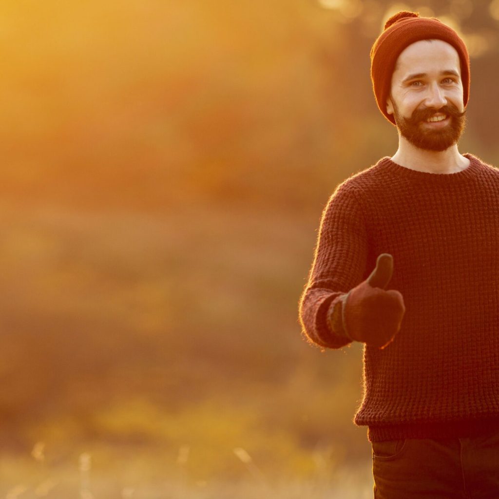 Smiling man in warm clothes giving a thumbs-up during sunset, symbolizing positivity and men's health